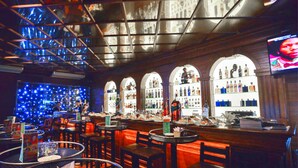 A bar with multiple seating areas, a television screen, and a variety of bottles on shelves. - Halong Palace Hotel (Bai Chay)