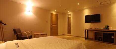 A hotel room with a bed, a desk, a chair, a TV, and a door.