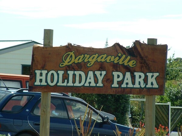 A wooden sign for Dargaville Holiday Park with text and a damaged edge.