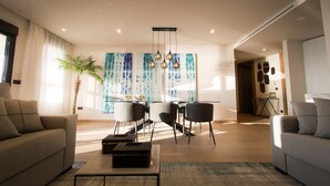 Ein modernes Wohnzimmer mit Sofa, Couchtisch und Essbereich mit Stühlen und einer Deckenleuchte.