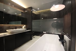 Un baño moderno con una bañera blanca grande, una ducha con cerramiento de vidrio y un mueble de tocador oscuro con un espejo grande.