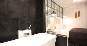 Un baño moderno con un espejo grande, un lavamanos blanco y una pared revestida de baldosas oscuras.