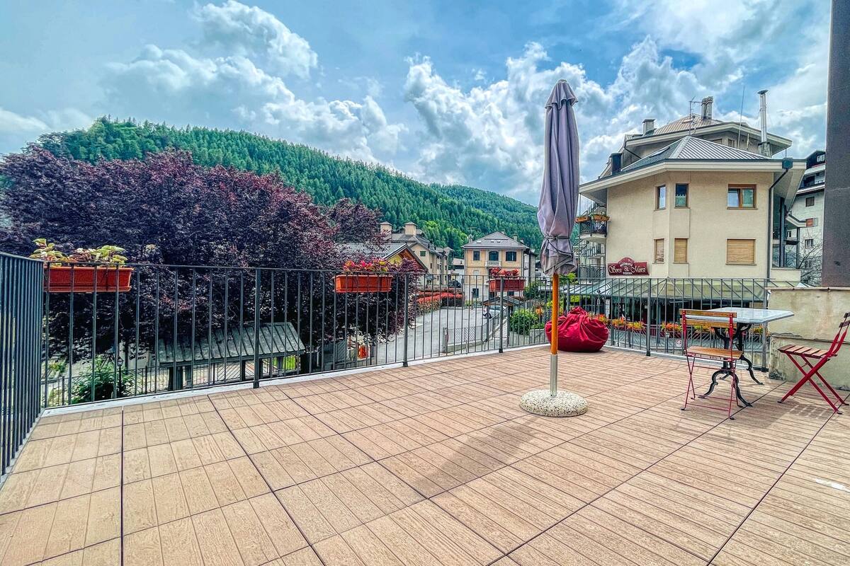 A terrace with a tiled floor, a red bean bag, a table, and an umbrella.