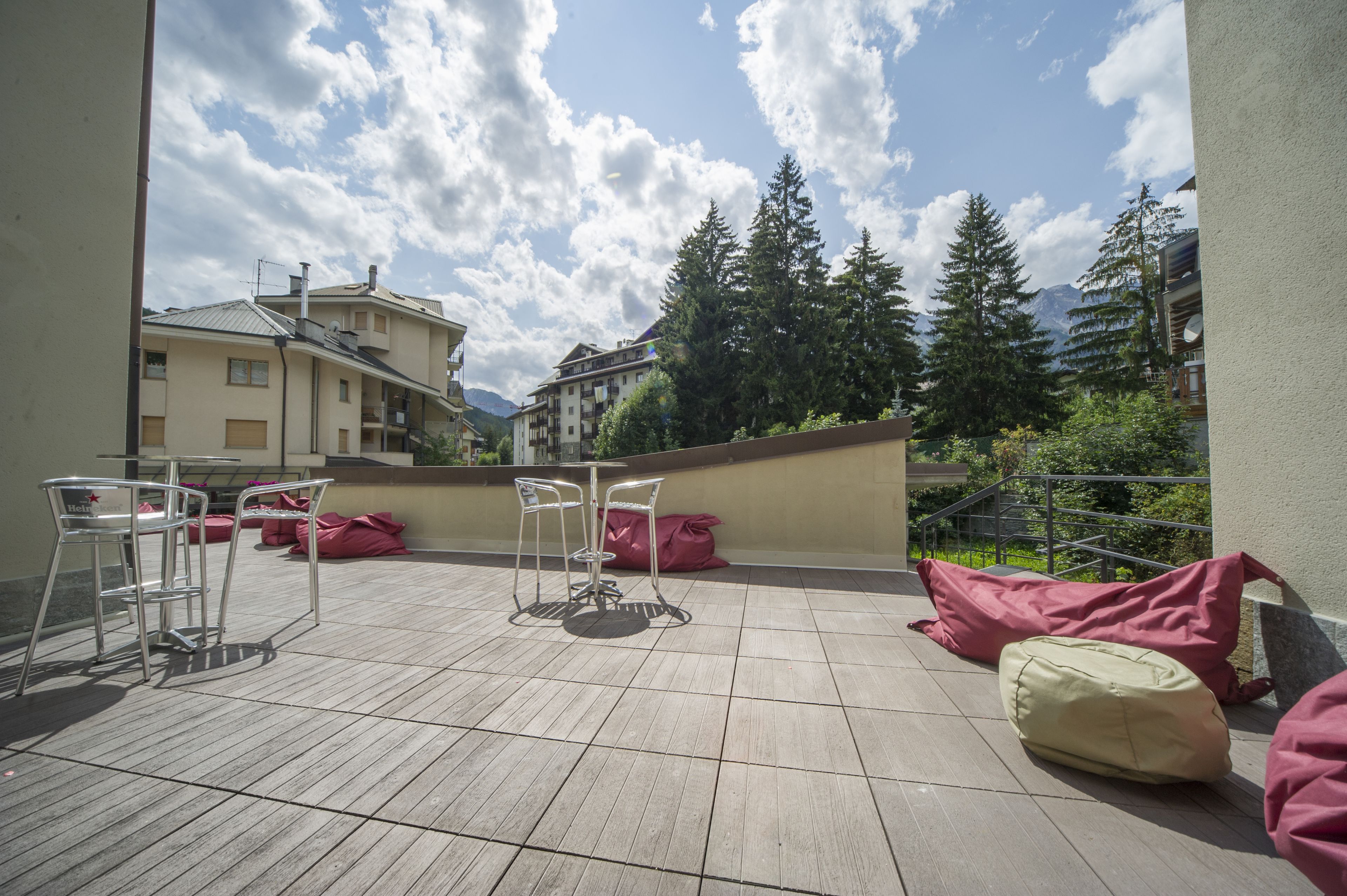 A terrace with a table and chairs, red bean bags, and a view of buildings and trees.