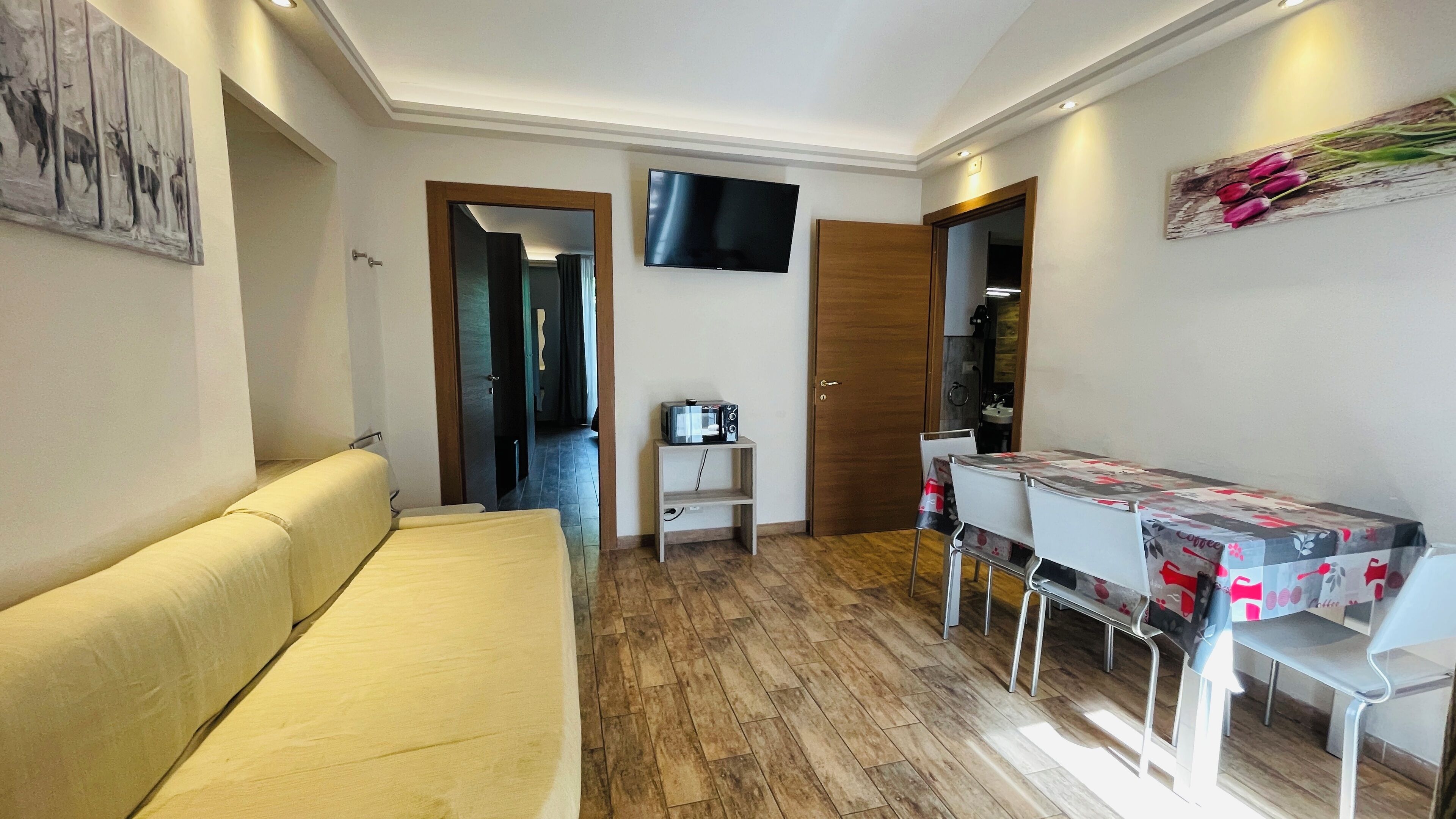 Un espacio habitable compacto con un sofá, una pequeña mesa con sillas, un televisor montado en la pared y suelo de madera.
