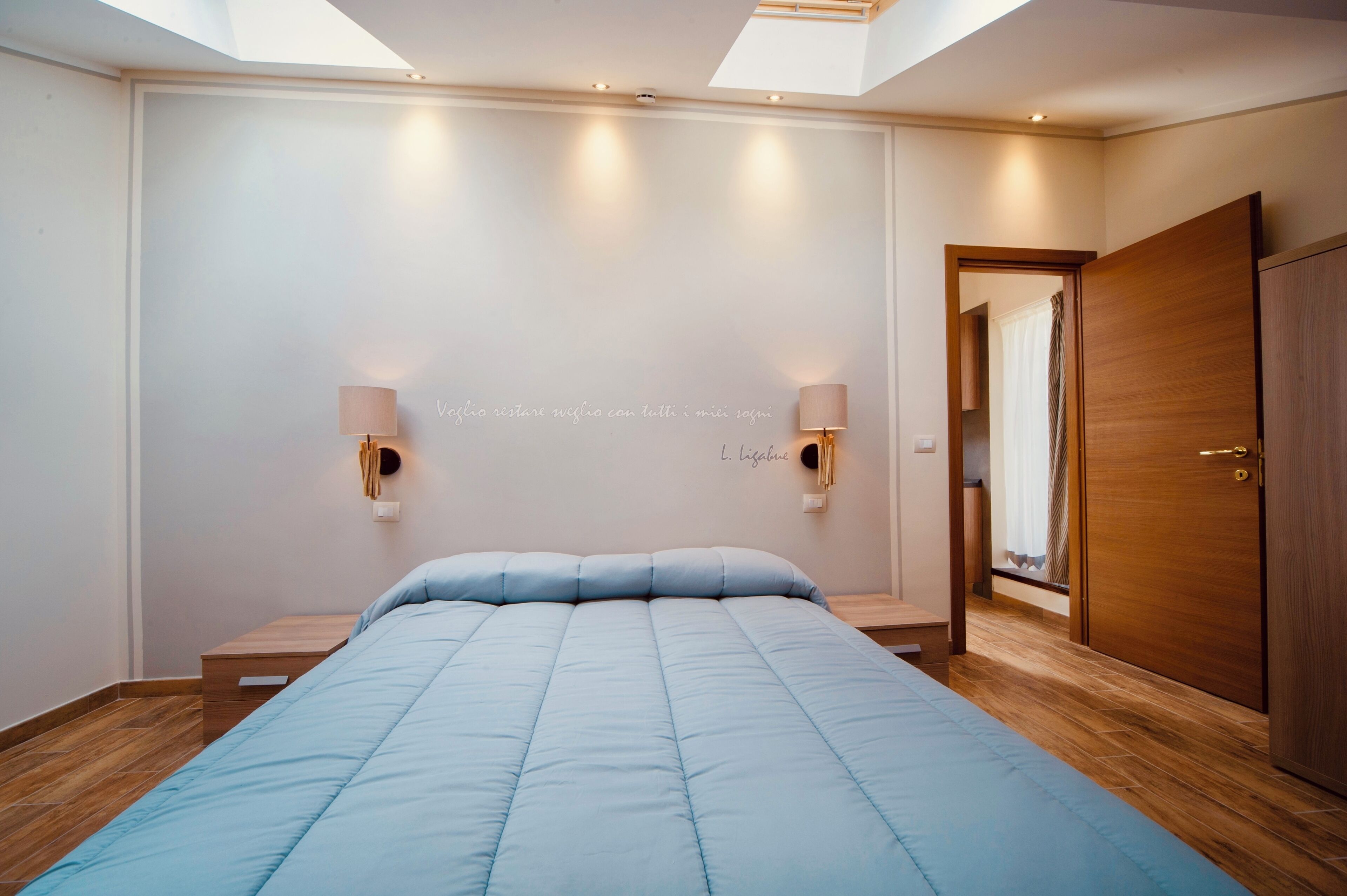 Un dormitorio con una cama, dos lámparas de pared, un armario de madera y un tragaluz.