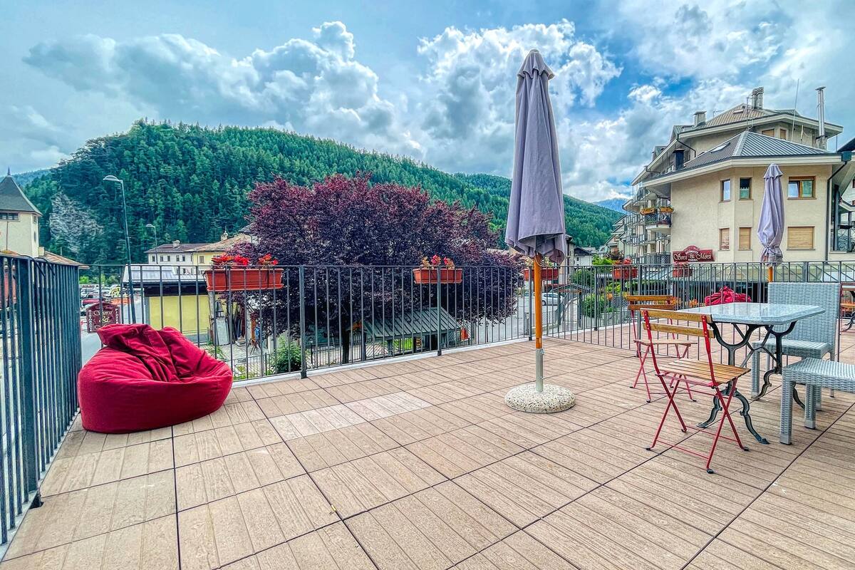 A terrace with a red bean bag, a table with chairs, and a purple umbrella.