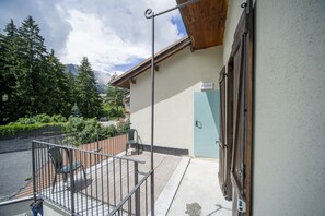 Un balcon doté d’une rambarde en métal, d’une porte en bois et offrant une vue sur les arbres et les montagnes.