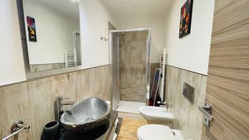 Een moderne badkamer met een wastafel van natuursteen, een toilet en een douche.