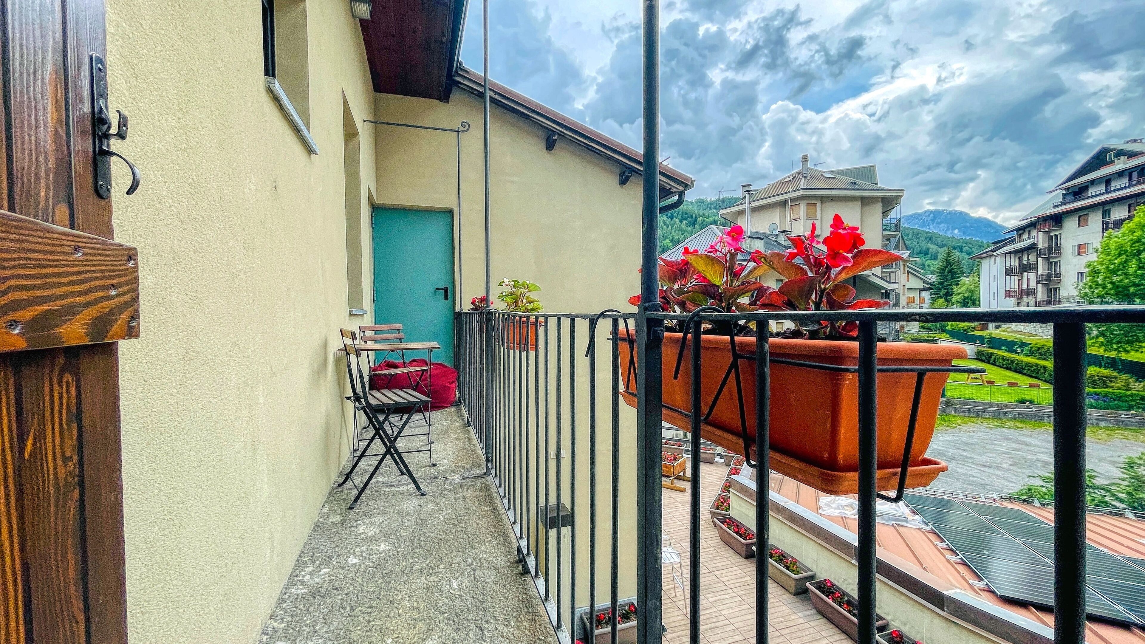 A balcony with a wooden chair, a red bag, and potted plants.