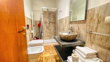 Une salle de bain moderne avec un lavabo en pierre, un bidet, une douche et un porte-serviettes.