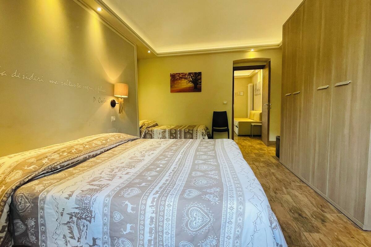 A hotel room with a large bed, a wardrobe, a seating area with chairs, and a painting on the wall.