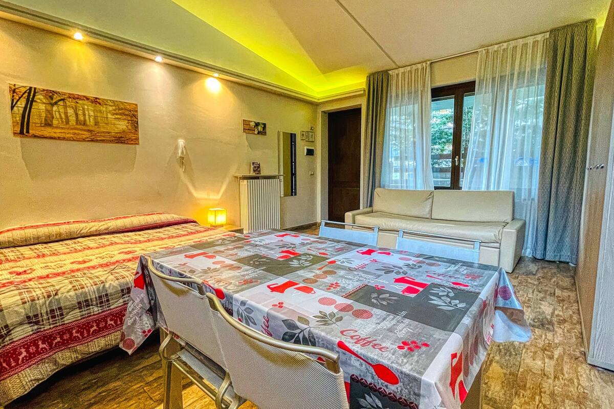 A cozy room with two beds, a sofa, a dining table, and a window with curtains.