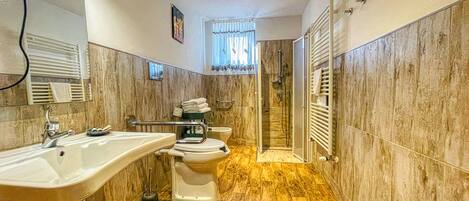 A bathroom with a sink, toilet, and shower area, featuring marble walls and wooden flooring.