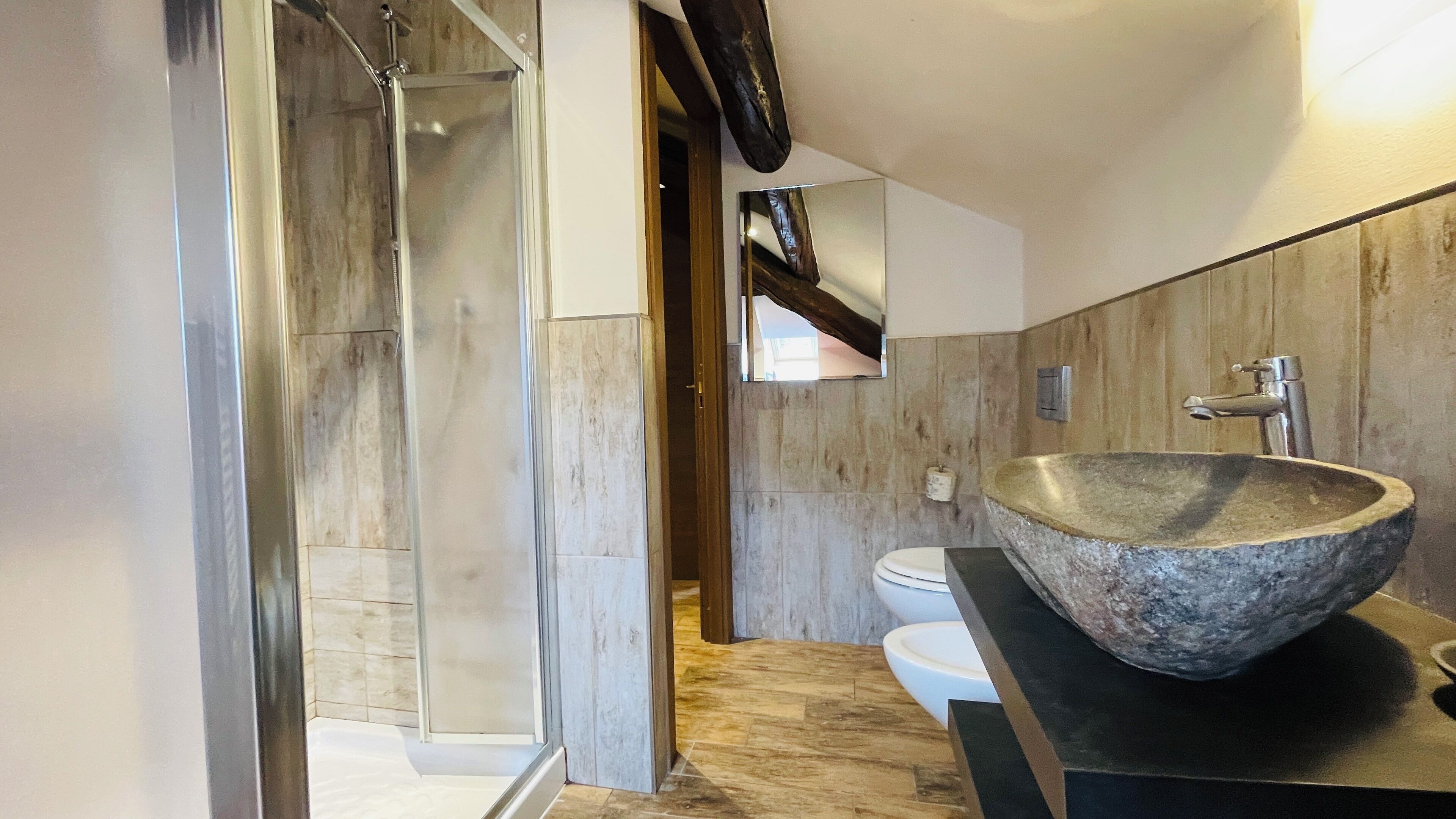 Un baño moderno con un lavamanos de piedra grande, una cabina de ducha de vidrio y una pared decorativa de madera.