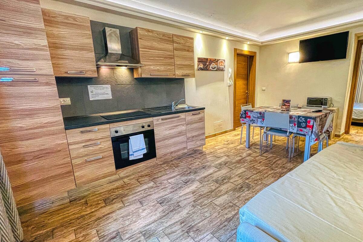 A compact kitchen with wooden cabinets, a built-in oven, and a dining area with a table and chairs.