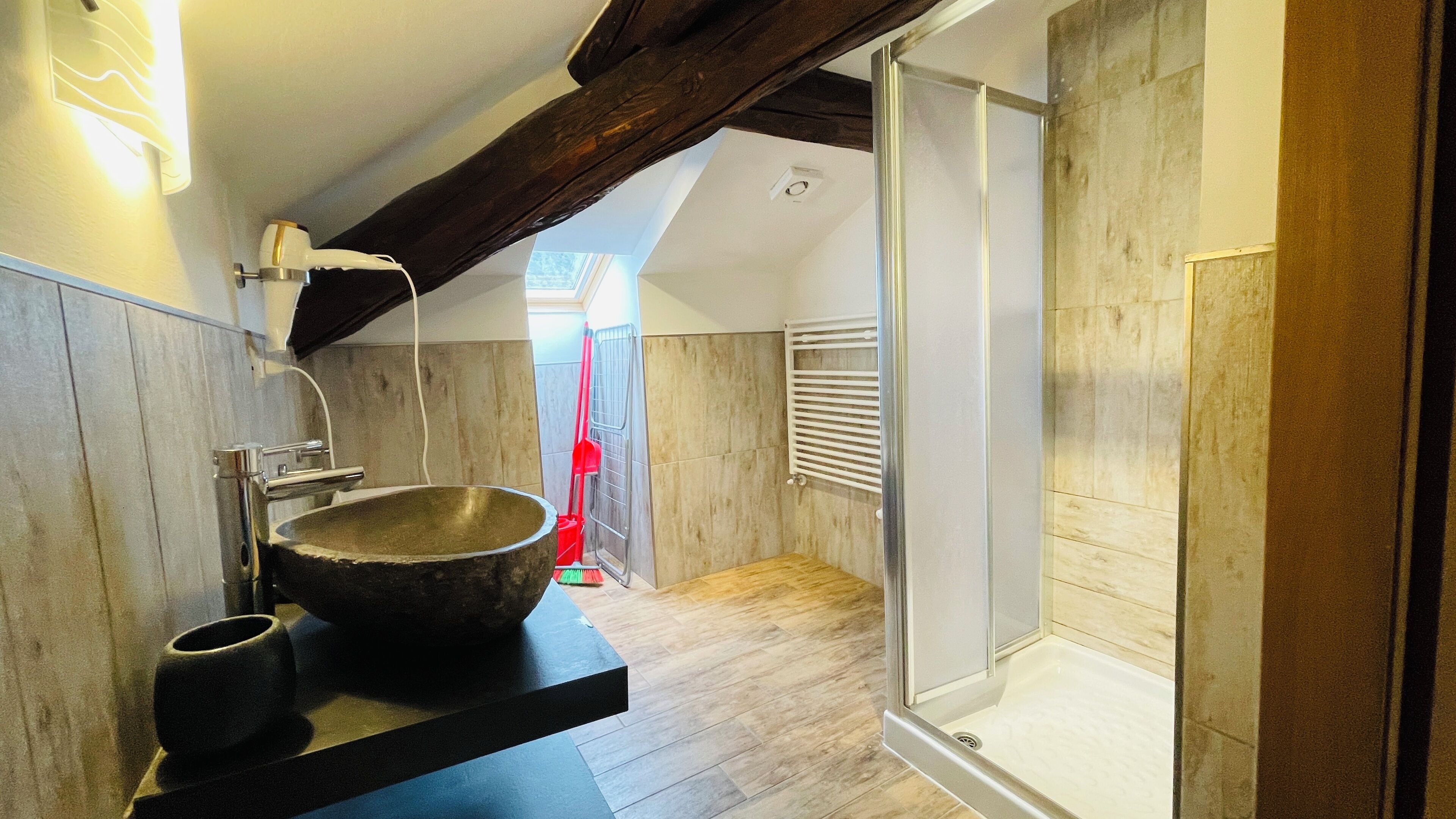 Un baño moderno con un lavabo de piedra grande, una ducha con puertas de vidrio y suelo de madera.