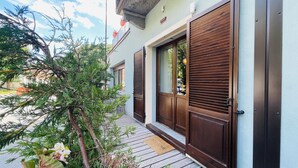 Un edificio moderno con contraventanas de madera, un felpudo y un pequeño porche con plantas en macetas.