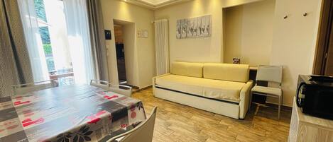 A room with a dining table, a sofa, a chair, a lamp, and a television.