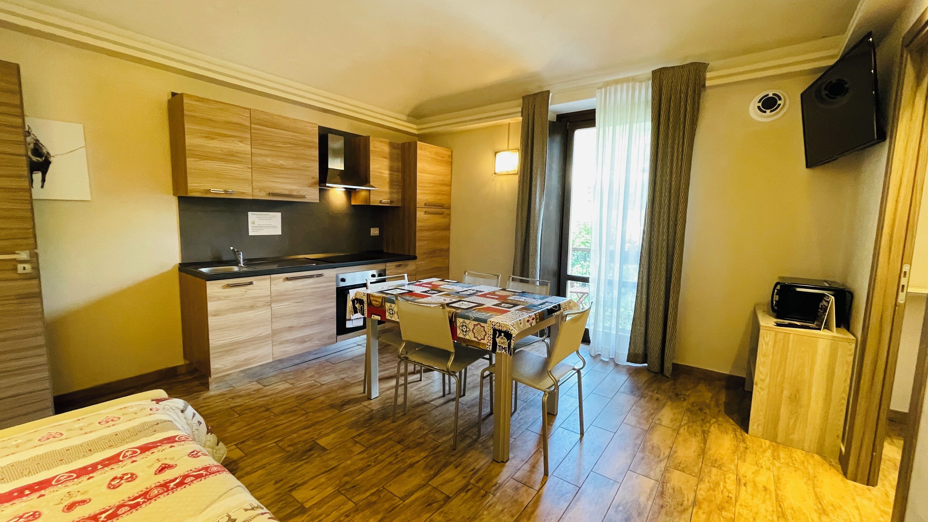 A compact hotel room with a kitchenette, a dining area with a table and chairs, and a bed.