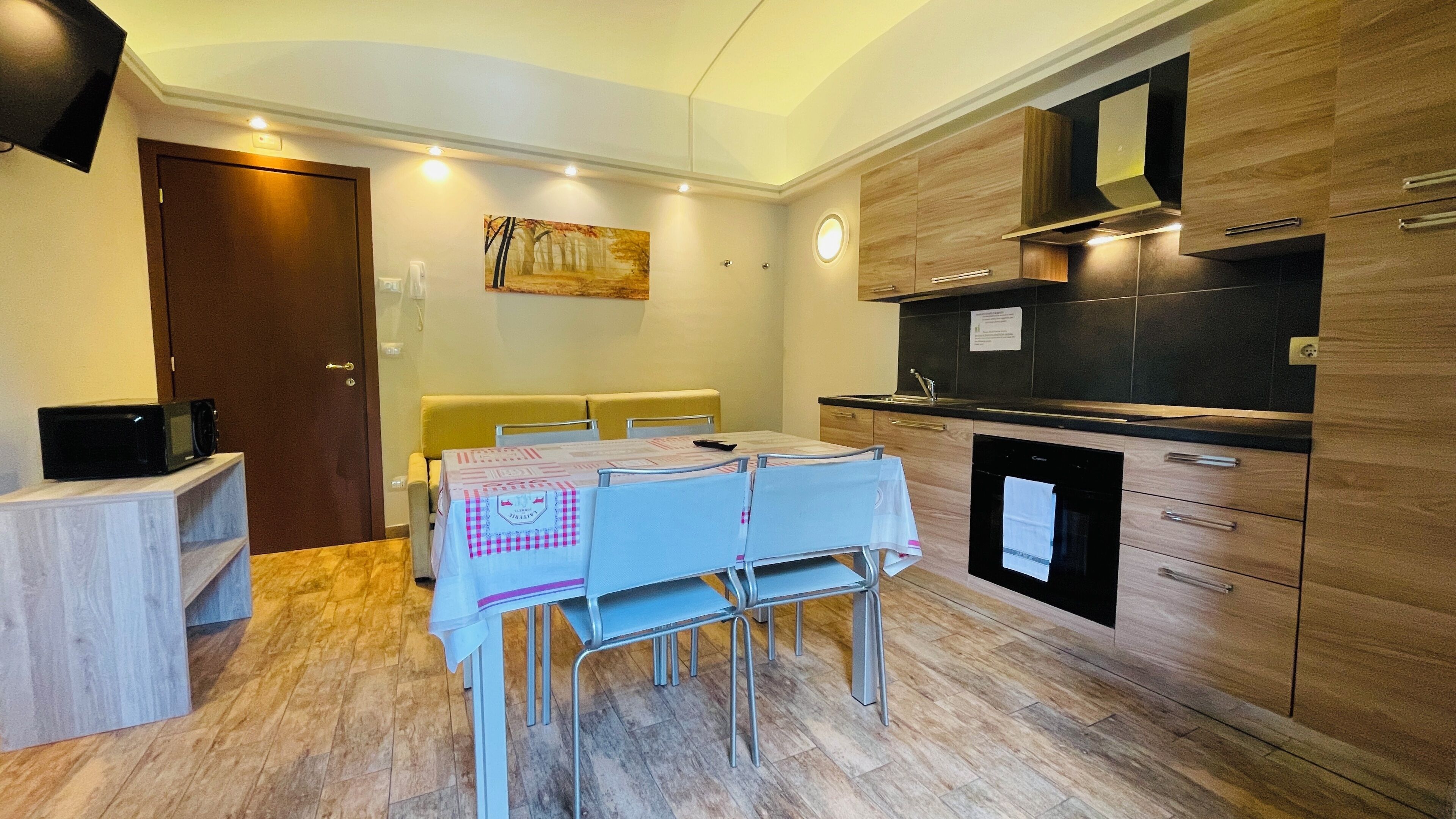 A compact kitchen with a microwave, a dining table with chairs, and a wooden cabinet with a built-in oven.