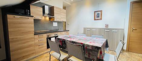 A compact kitchen with wooden cabinets, a built-in oven, and a dining table with chairs.