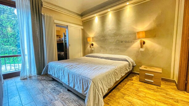 Un dormitorio con una cama grande, dos lámparas fijadas a la pared, vista a un balcón y una cita en la pared.
