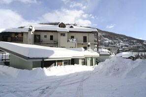 Un immeuble à plusieurs étages, doté d’un toit en pente recouvert de neige, entouré d’un paysage enneigé et avec une montagne en arrière-plan.