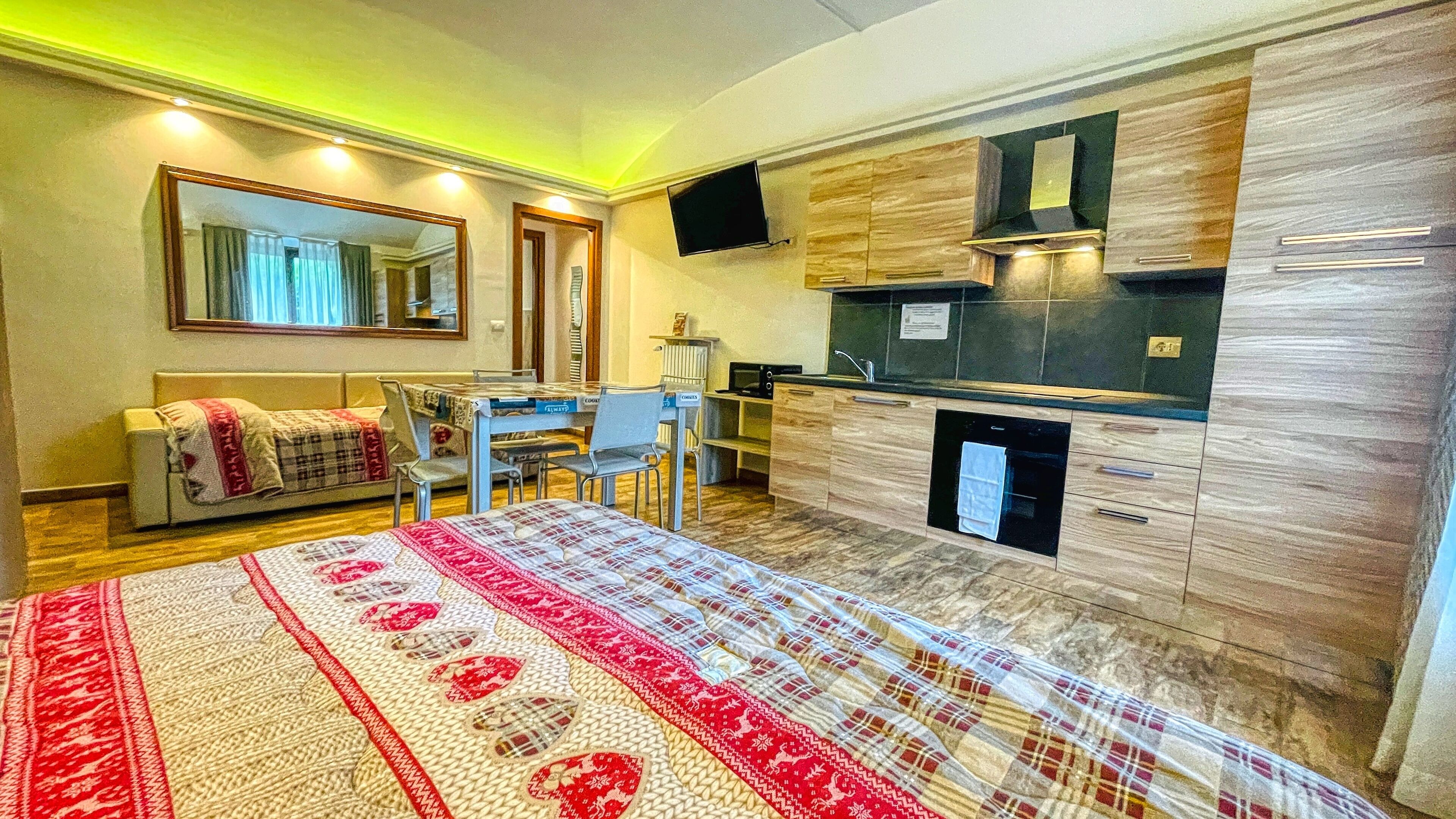Une chambre d’hôtel de taille réduite, comprenant un lit, un bureau, une chaise, un coin cuisine et un miroir.