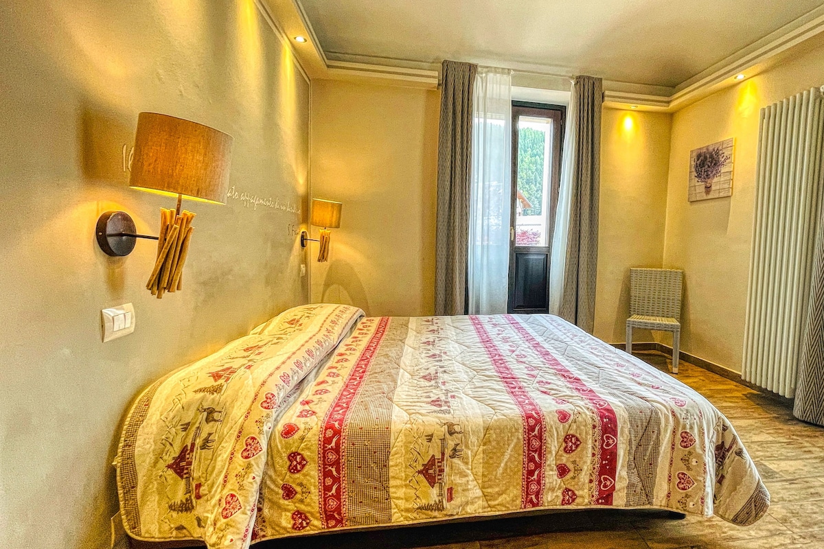 Un dormitorio con cama, una silla, una ventana con cortinas y una lámpara fijada a la pared.