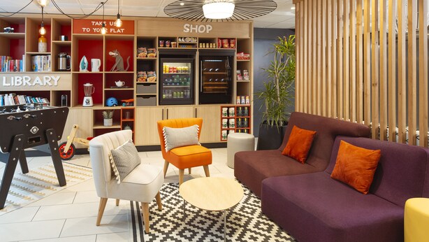 A modern interior with a flat-screen TV, a sofa, a coffee table, a bookshelf, and a shop area. - Aparthotel Adagio Access Dijon République (Dijon)