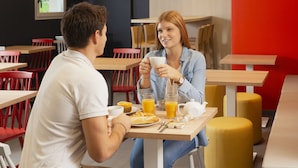 A café with wooden tables and red chairs, a yellow ottoman, and a red wall. - Aparthotel Adagio Access Dijon République (Dijon)