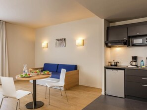 A compact kitchen with a microwave, coffee maker, and dishwasher. There is a blue sofa and a dining table with chairs. - Aparthotel Adagio Access Dijon République (Dijon)