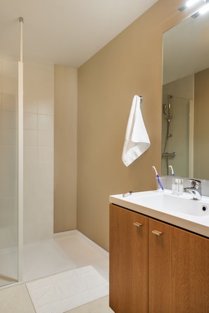 Un baño moderno con ducha, lavabo con espejo y mueble de madera.
