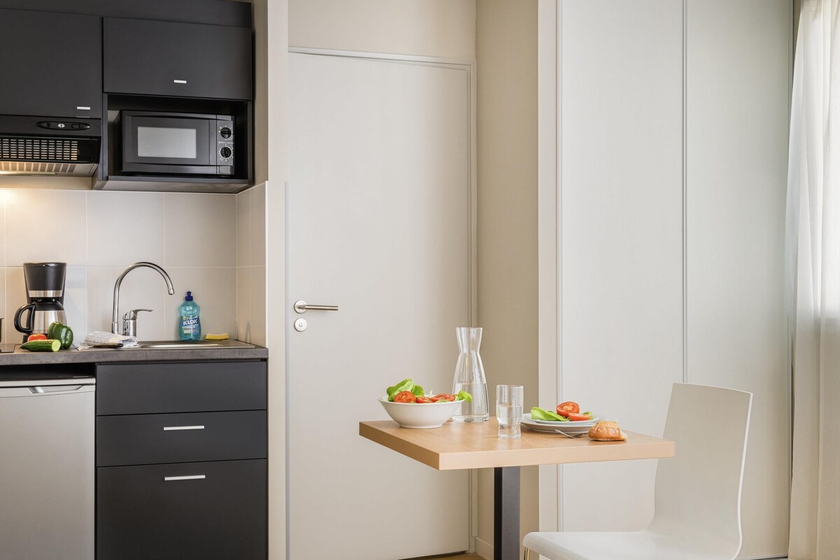A compact kitchen with a microwave, coffee maker, and a small dining table with a chair.