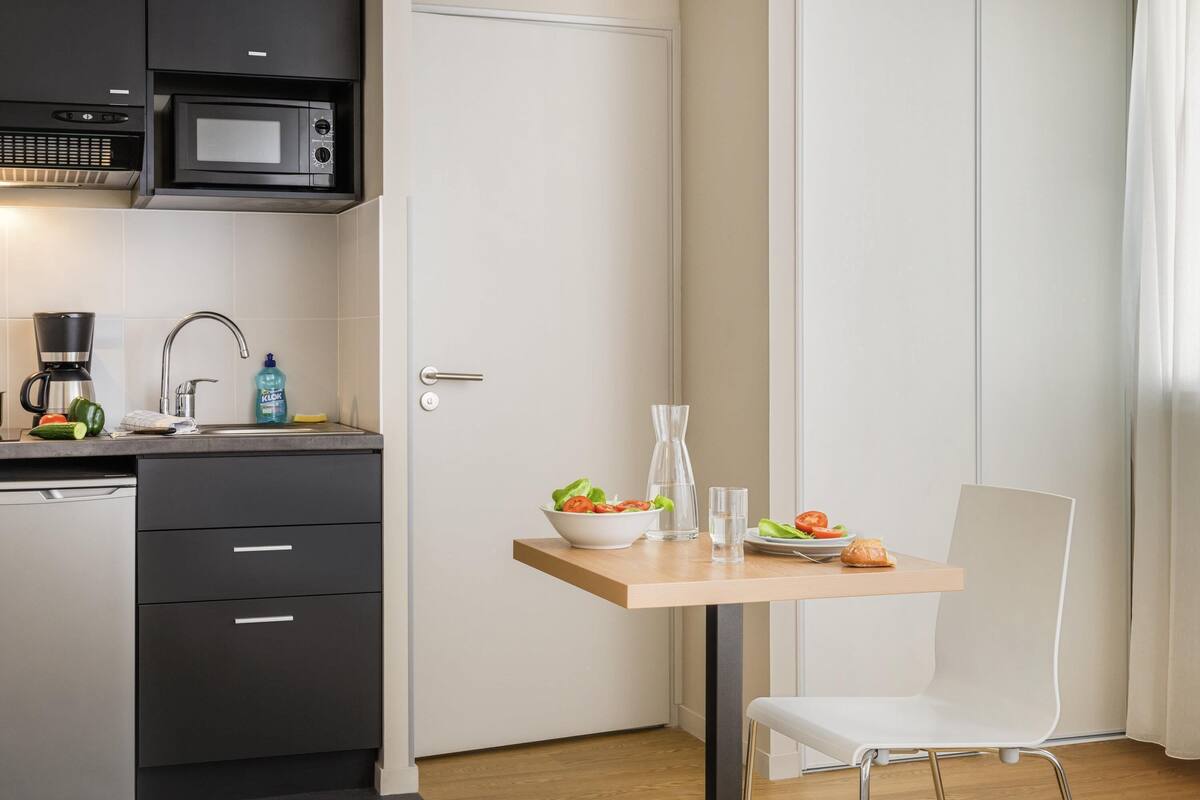 A compact kitchen with a microwave, coffee maker, and a small dining table with a chair.