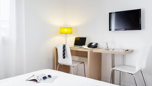 A hotel room with a desk, two chairs, a TV, a lamp, and a bed. - Aparthotel Adagio Access Nancy Centre (Nancy)