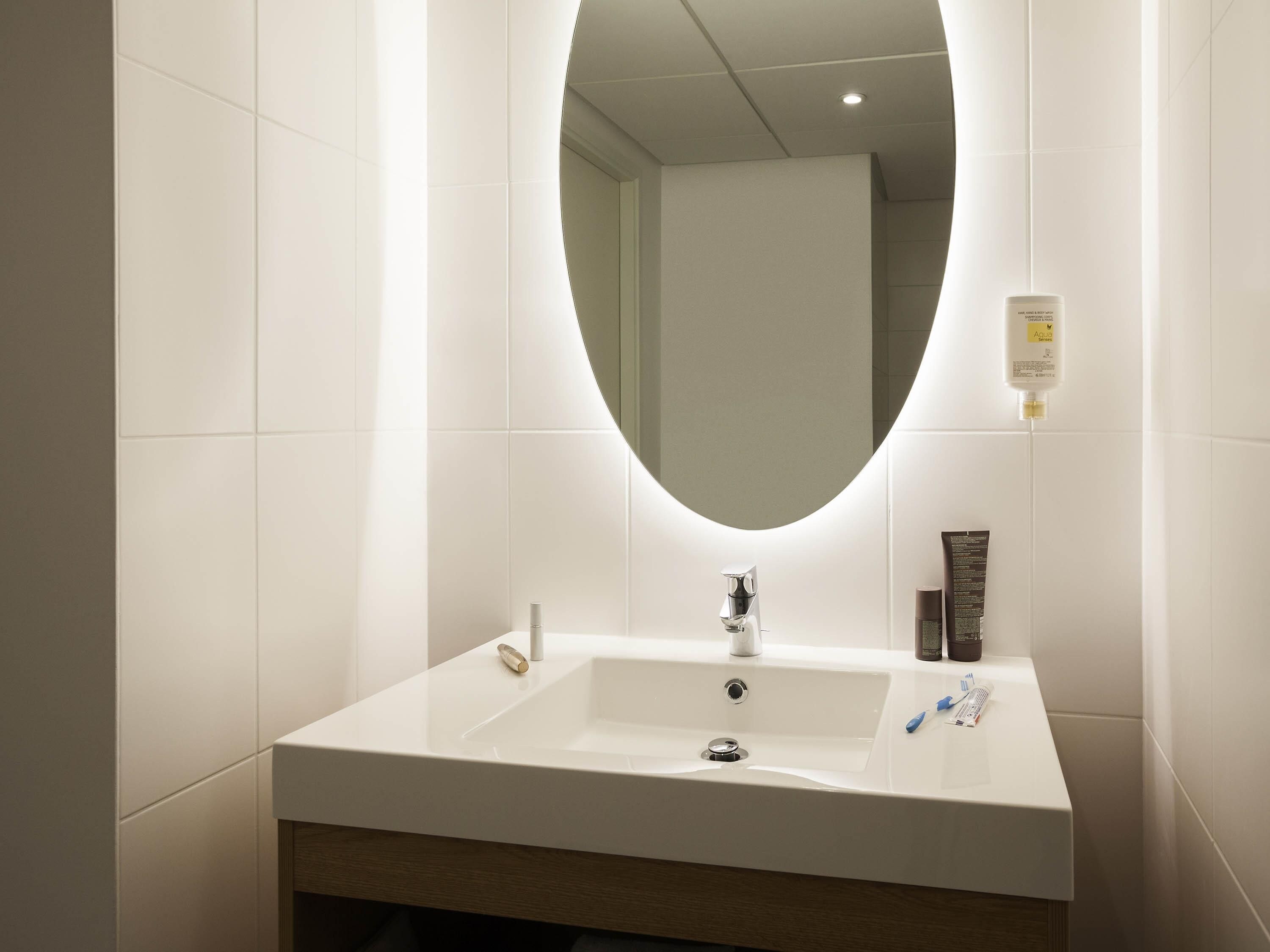 A modern bathroom with a white sink, a mirror, and toiletries on the wall.