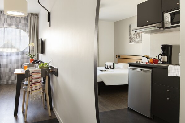 Habitación de hotel pequeña con kitchenette, una cama, un comedor con mesa y sillas, y un baño compacto.