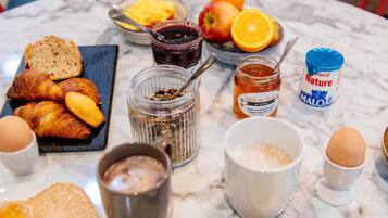 Una mesa de desayuno con cruasanes, pan, frutas, mermeladas, miel y una botella de miel.