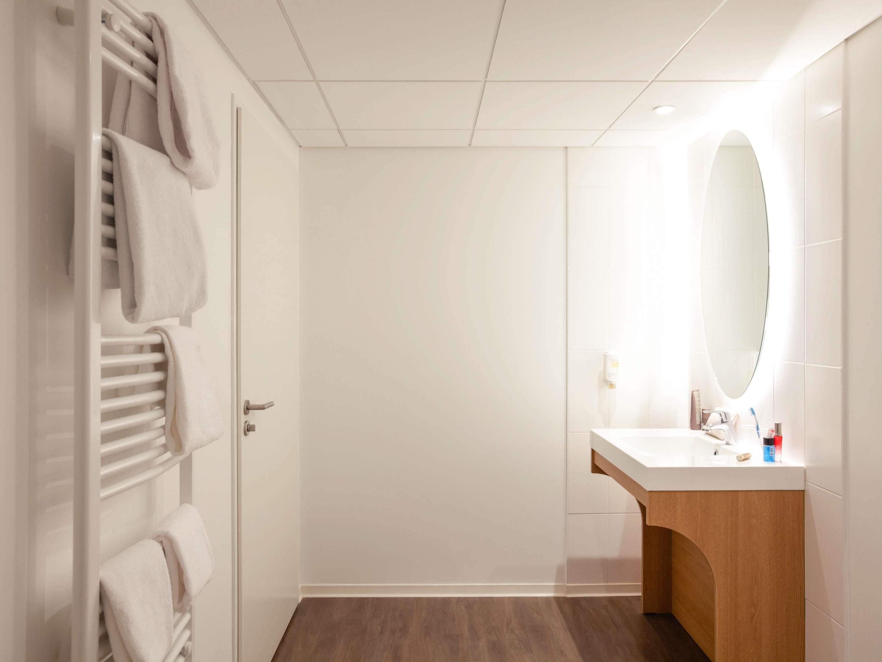 A modern bathroom with a white vanity, a large mirror, and a towel rack with towels.
