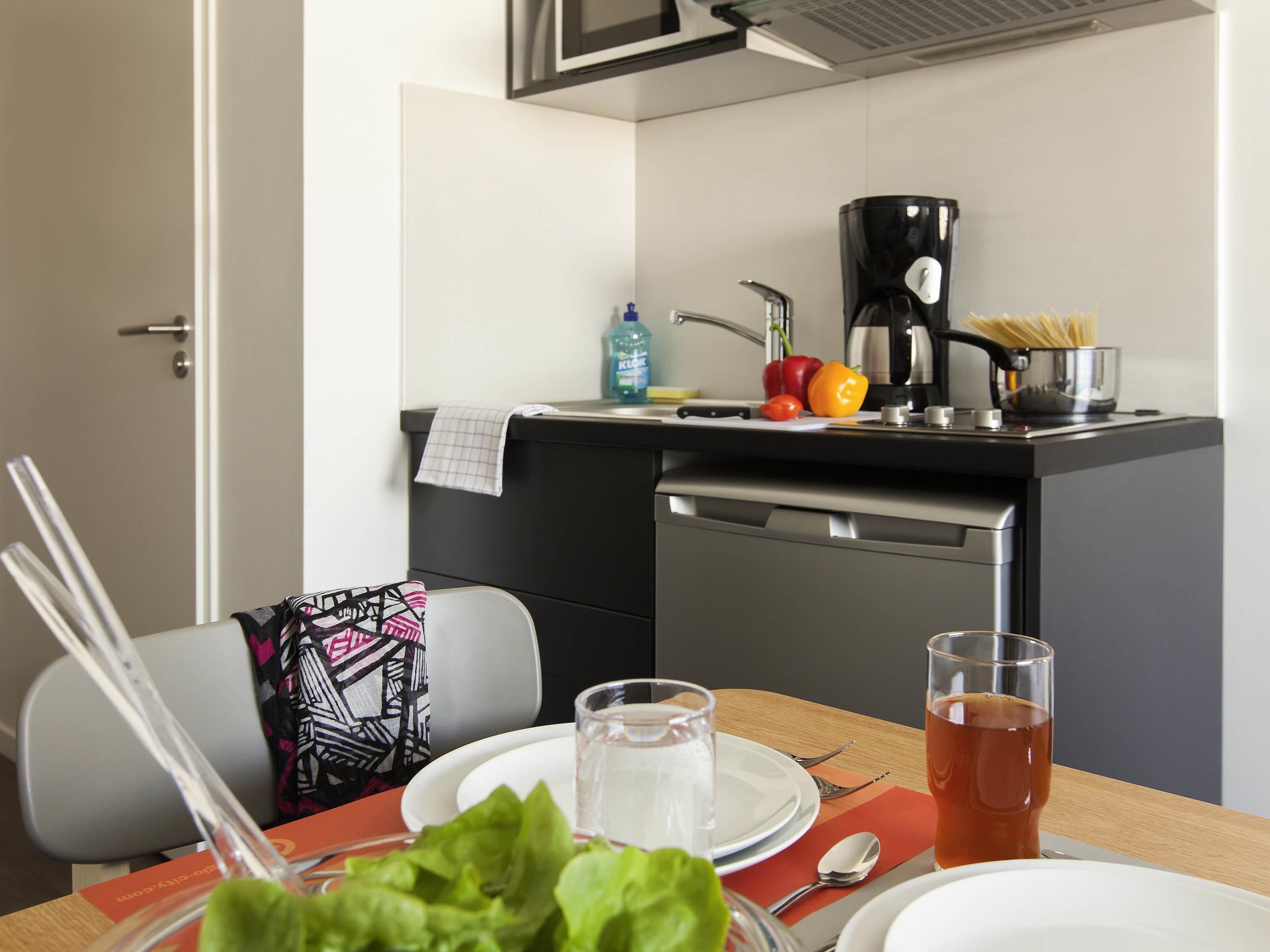 A modern kitchen with a coffee maker, a pot of spaghetti, and fresh vegetables on the counter.