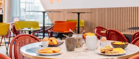 Comedor con mesas redondas, sillas rojas y diversos alimentos para el desayuno.