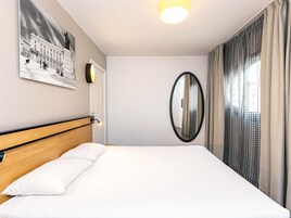 A hotel room with a bed, a wall-mounted mirror, a framed picture, and a window with curtains.