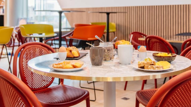 Comedor con mesas redondas, sillas rojas y diversos alimentos para el desayuno.