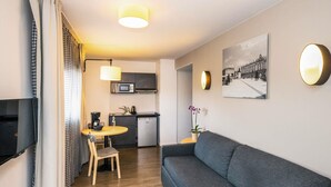 A compact living space with a sofa, dining table, chairs, a small kitchenette, and a television. - Aparthotel Adagio Access Nancy Centre (Nancy)