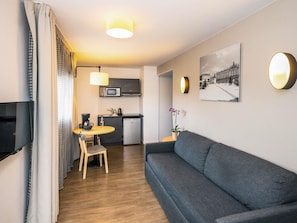 Un espacio habitable compacto con sofá, mesa de comedor, sillas, una kitchenette pequeña y televisión.