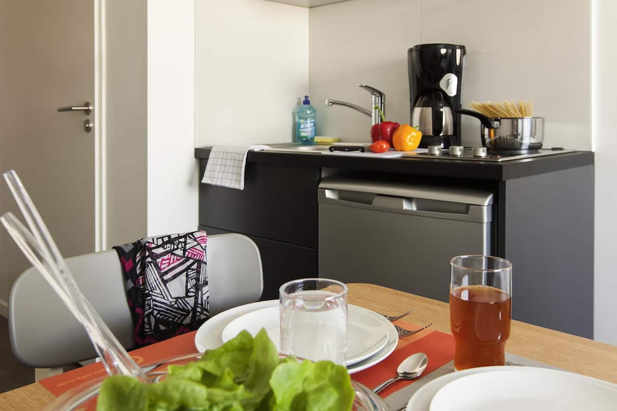 A modern kitchen with a coffee maker, a pot of spaghetti, and fresh vegetables on the counter.
