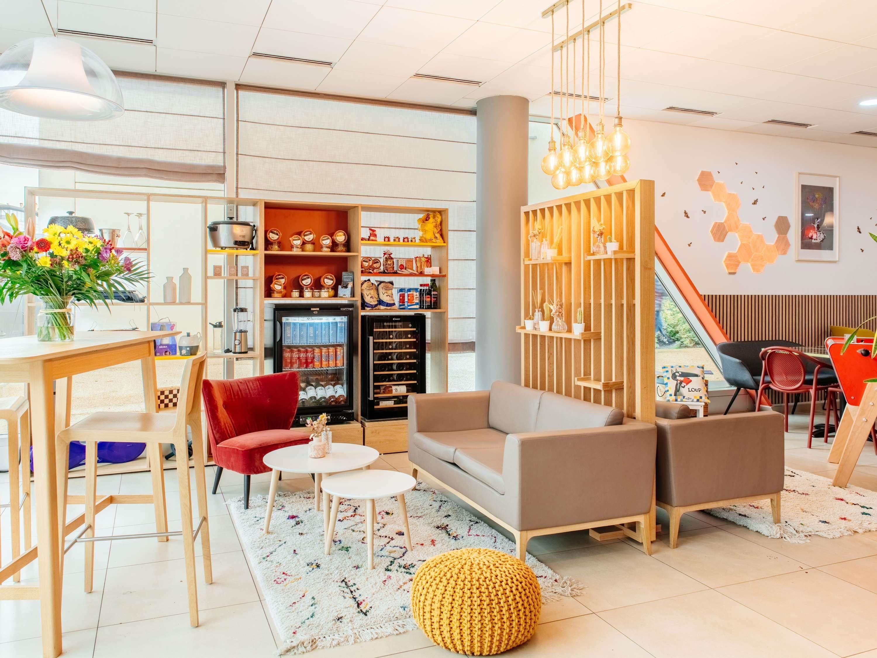 Ein modernes Interieur mit Sofa, Sesseln, einem Couchtisch, einem mit Getränken gefüllten Kühlschrank und einem Wandregal mit Dekoration.