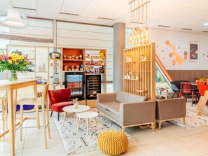 A modern interior with a sofa, chairs, a coffee table, a refrigerator stocked with beverages, and a wall-mounted shelf with decorative items. - Aparthotel Adagio Access Nancy Centre (Nancy)
